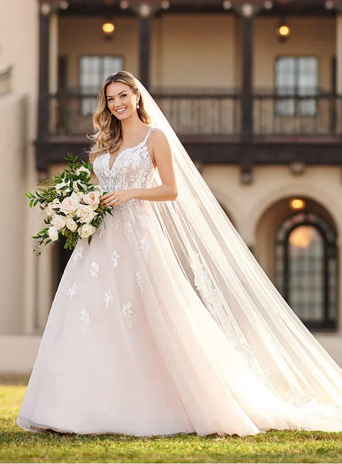 Bride in a white wedding dress with a long veil standing in front of a building.