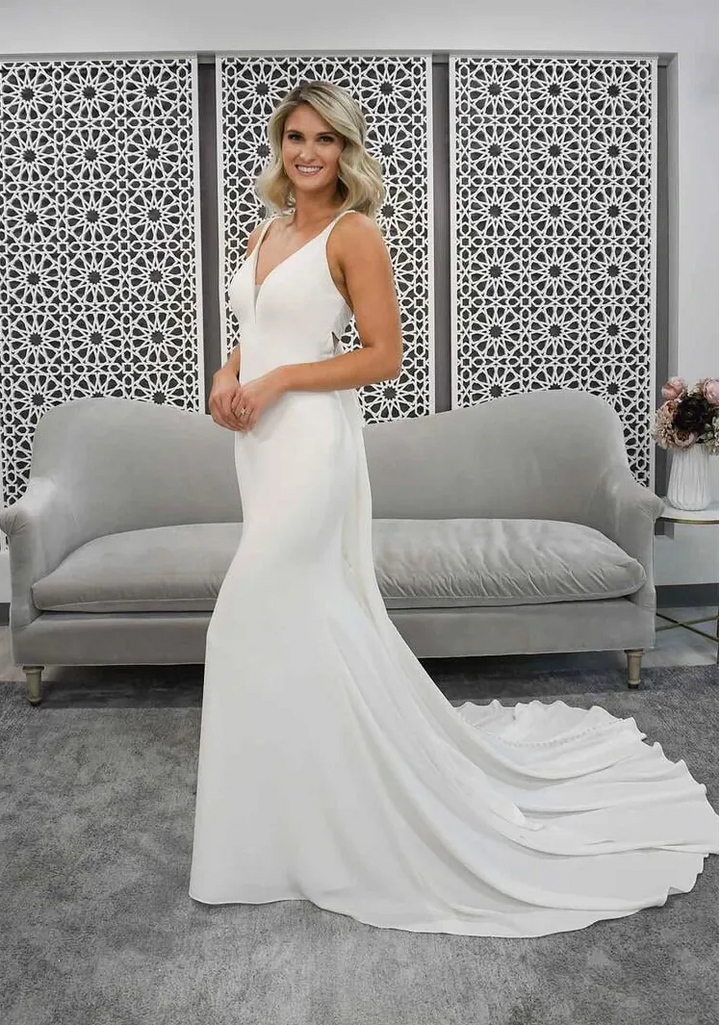 Woman in a white wedding dress standing in a room with gray couches and decorative wall.
