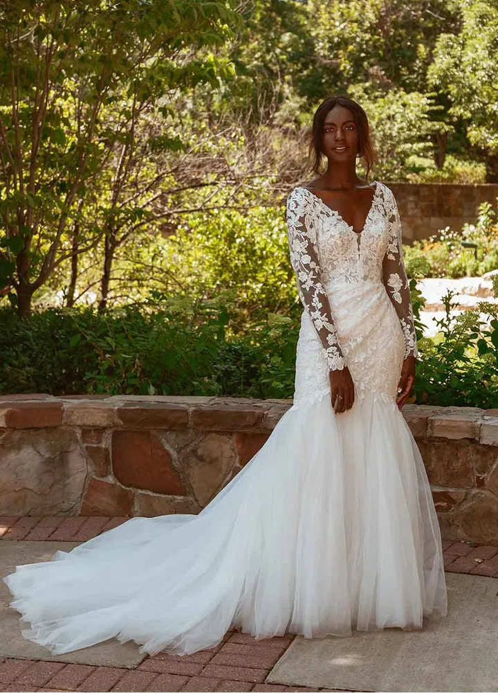 Woman in a white wedding dress standing outdoors with trees and a building in the background