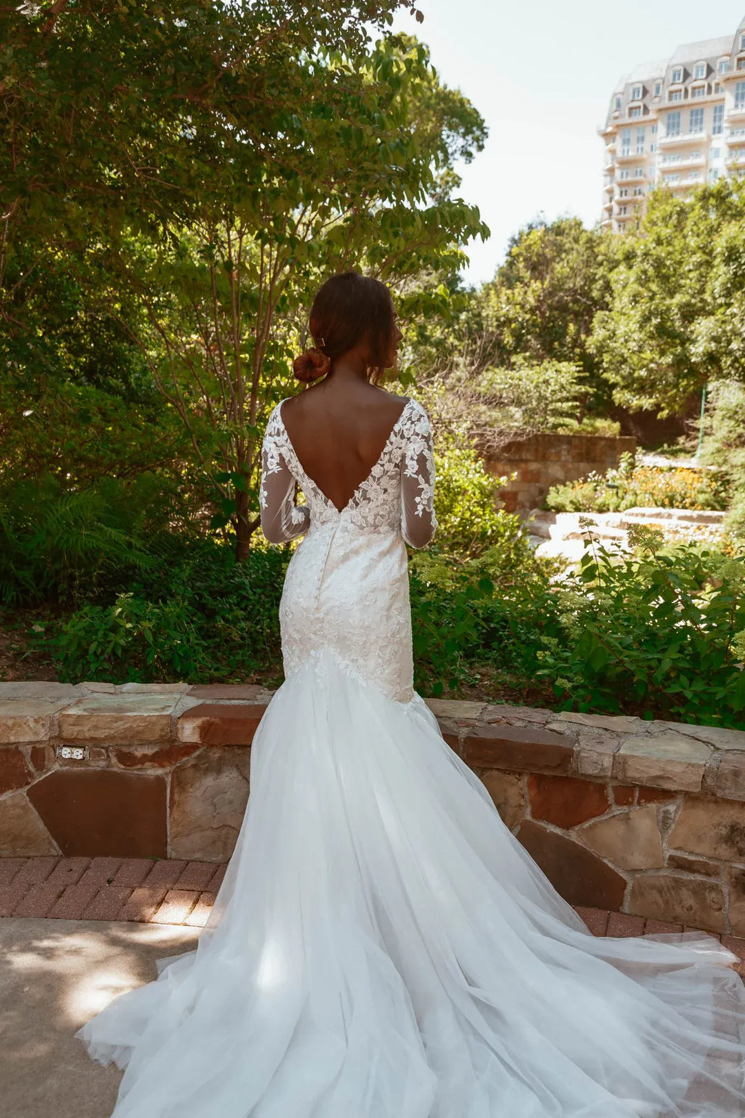 Woman in a white wedding dress with a low back standing in a garden.