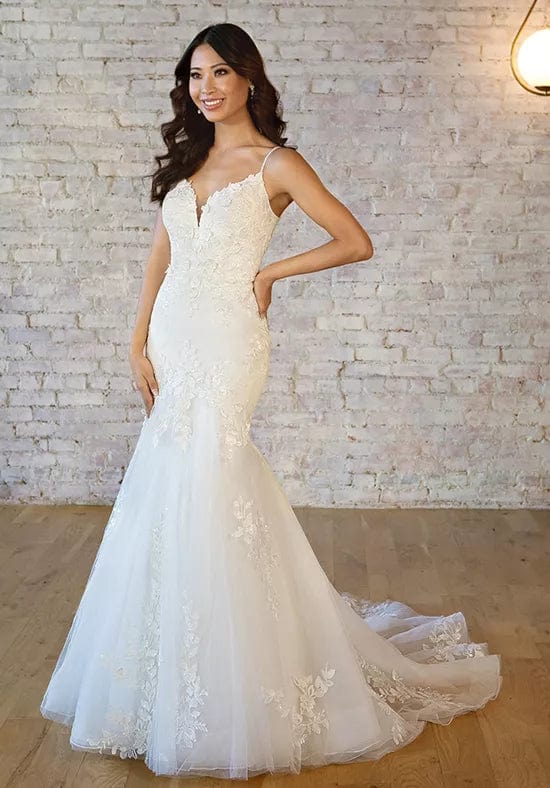 Woman wearing a white lace wedding dress against a light brick wall.