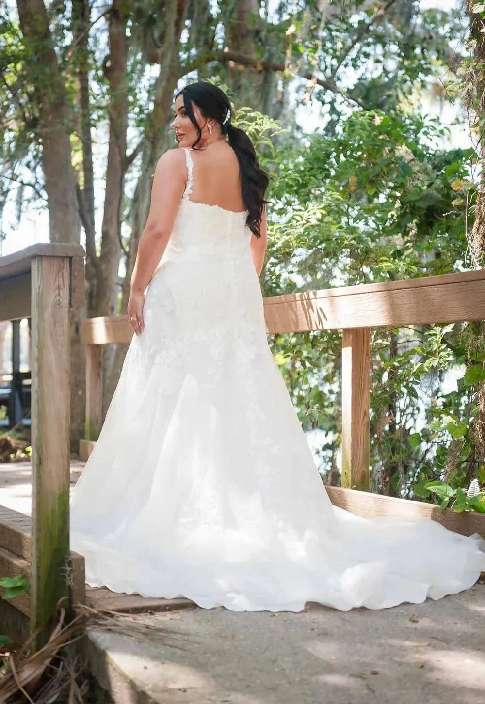 Woman in a white wedding dress standing on a wooden deck with trees in the background