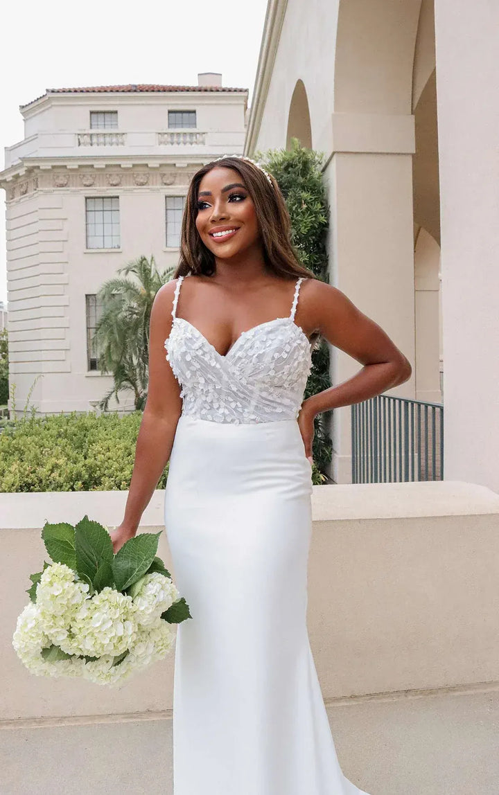 Woman in a white wedding dress holding a bouquet in front of a building.