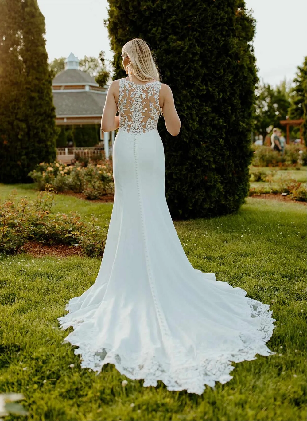 Woman in a white wedding dress with lace detailing standing in a garden.