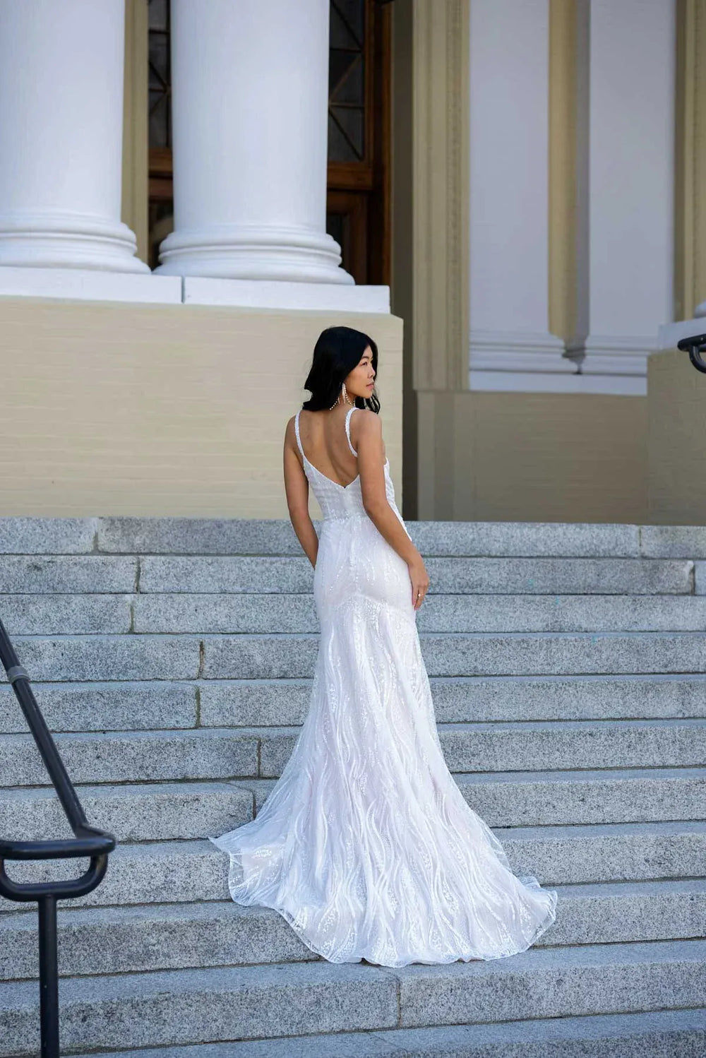 Woman in a white wedding dress standing on stone steps with classical architecture in the background