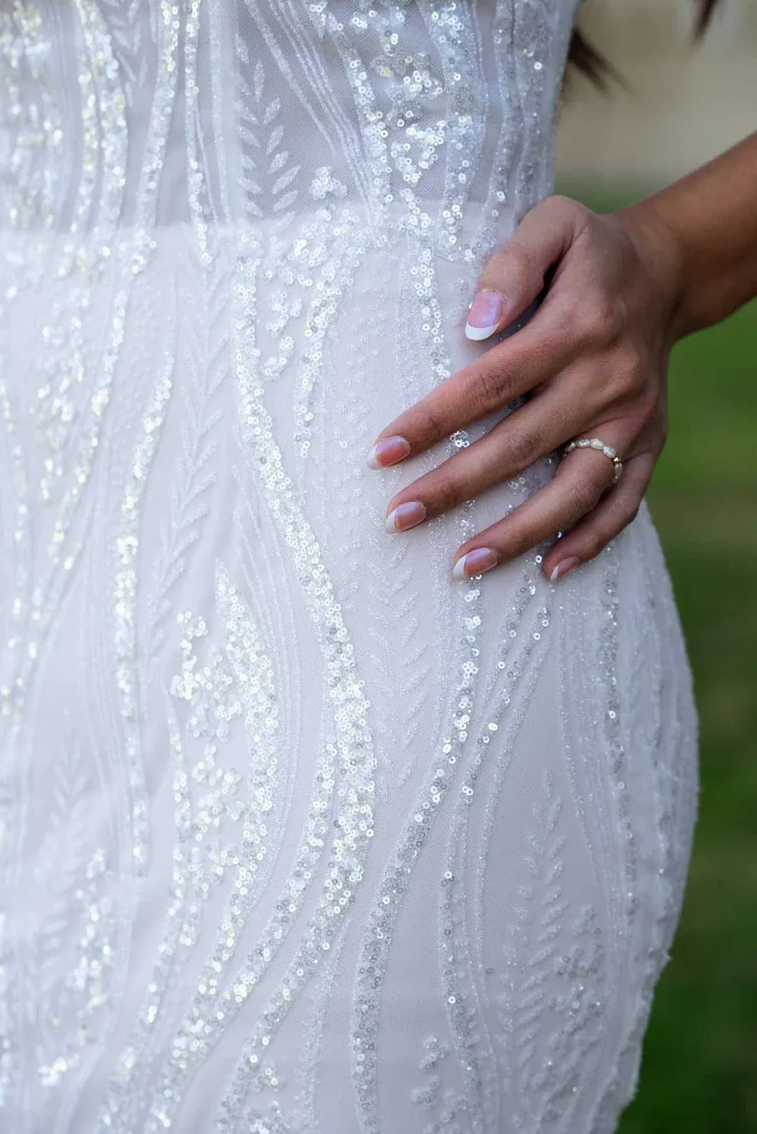 Close-up of a hand touching a sparkling white dress with a blurred green background