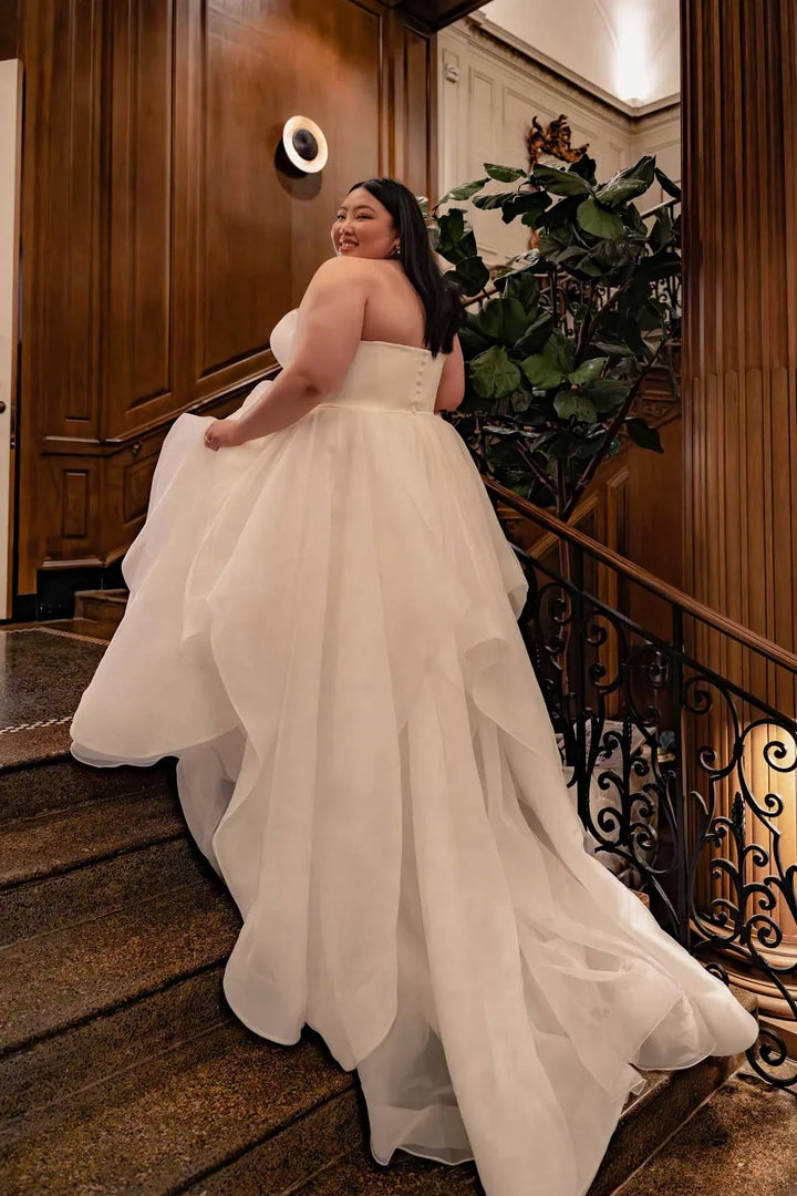 Woman in a white wedding dress standing in an elegant interior setting.