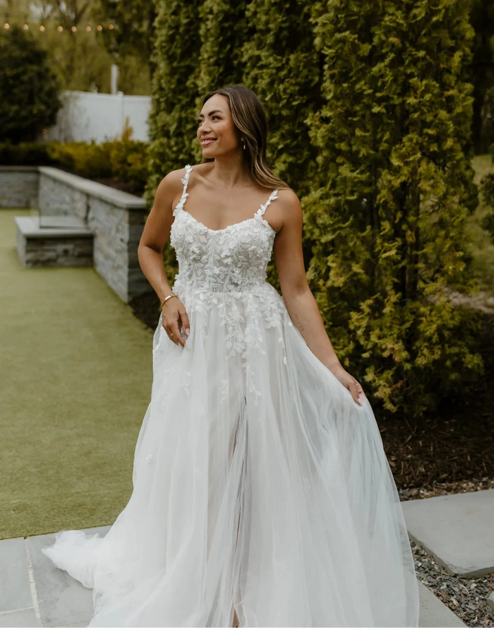 Woman in a white wedding dress standing outdoors with greenery in the background