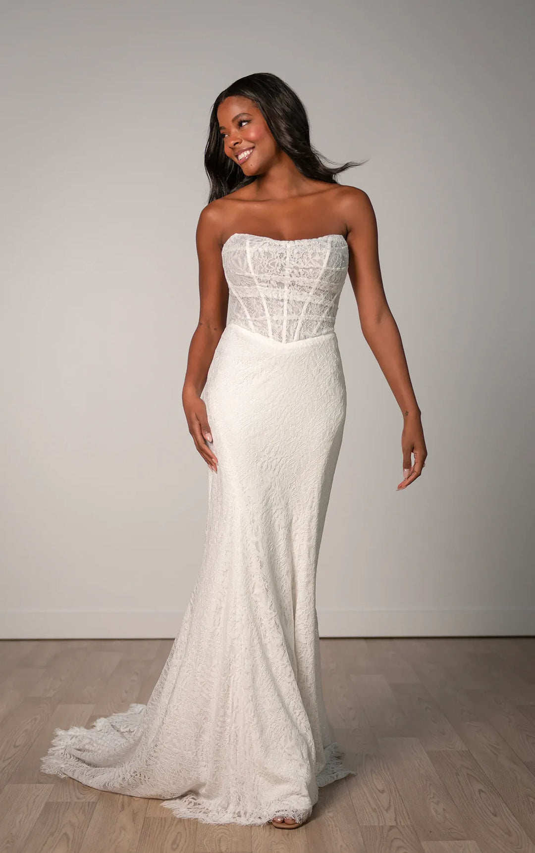 Woman wearing a white strapless wedding dress with lace detailing on a plain background