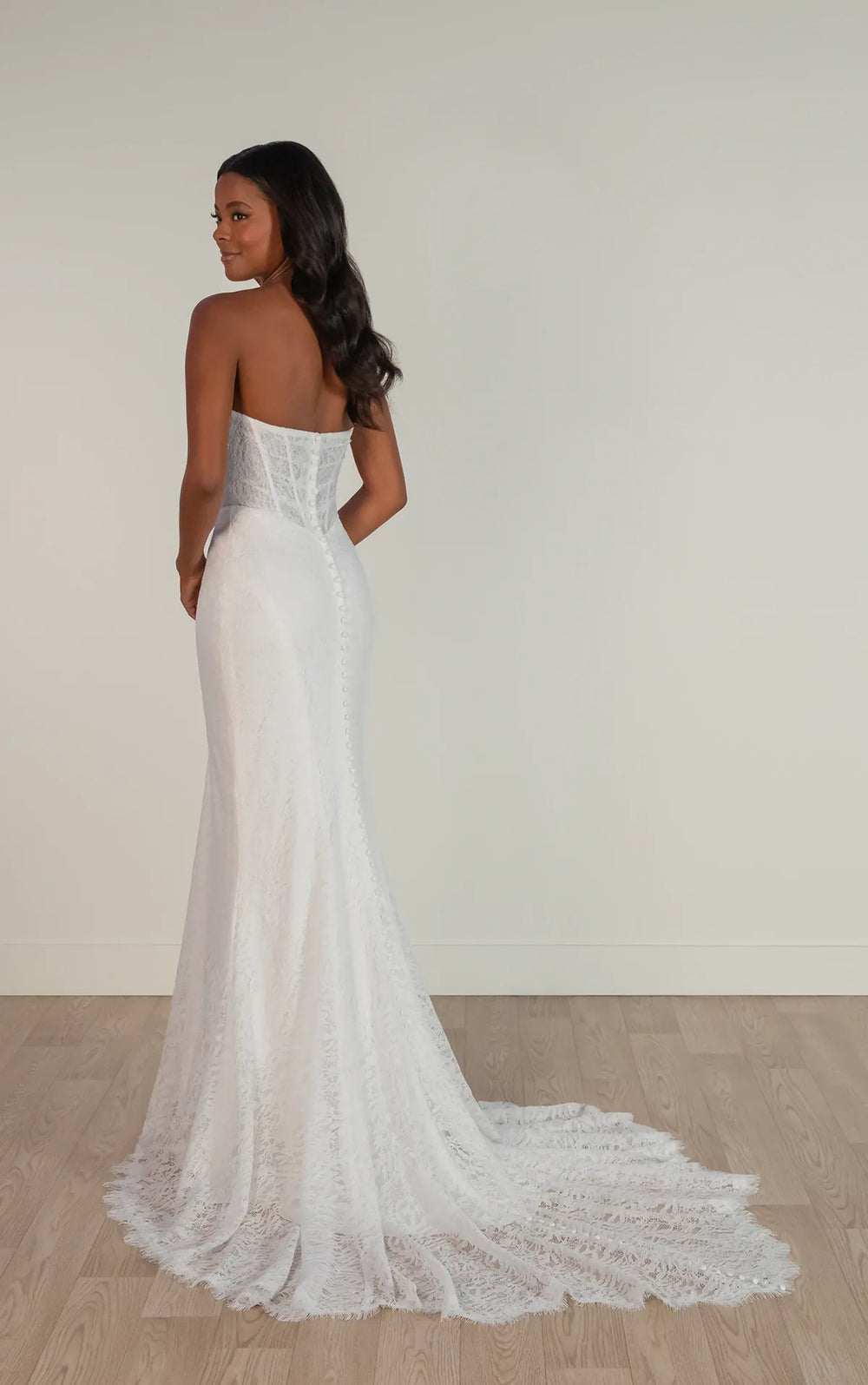 Woman wearing a white strapless lace wedding dress on a plain background