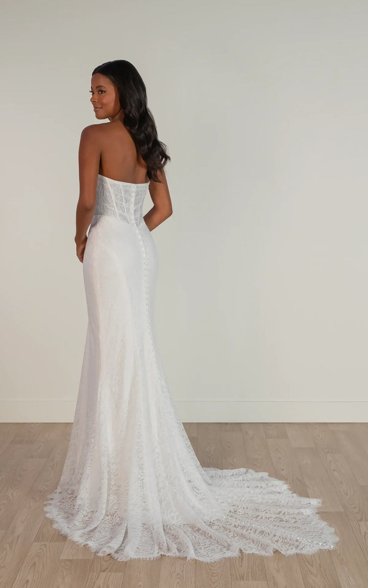 Woman wearing a white strapless lace wedding dress on a plain background