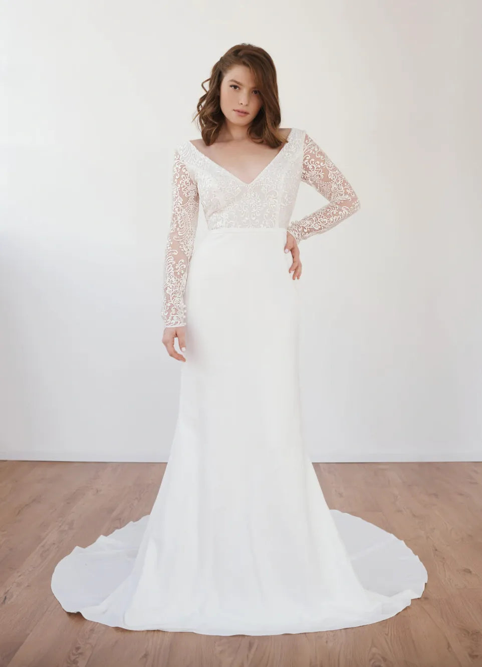 Woman wearing a white lace wedding dress with long sleeves on a wooden floor.