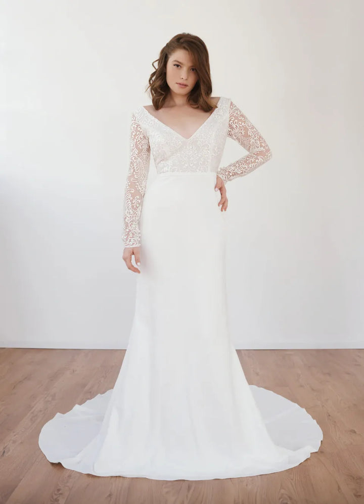Woman wearing a white lace wedding dress with long sleeves on a wooden floor.