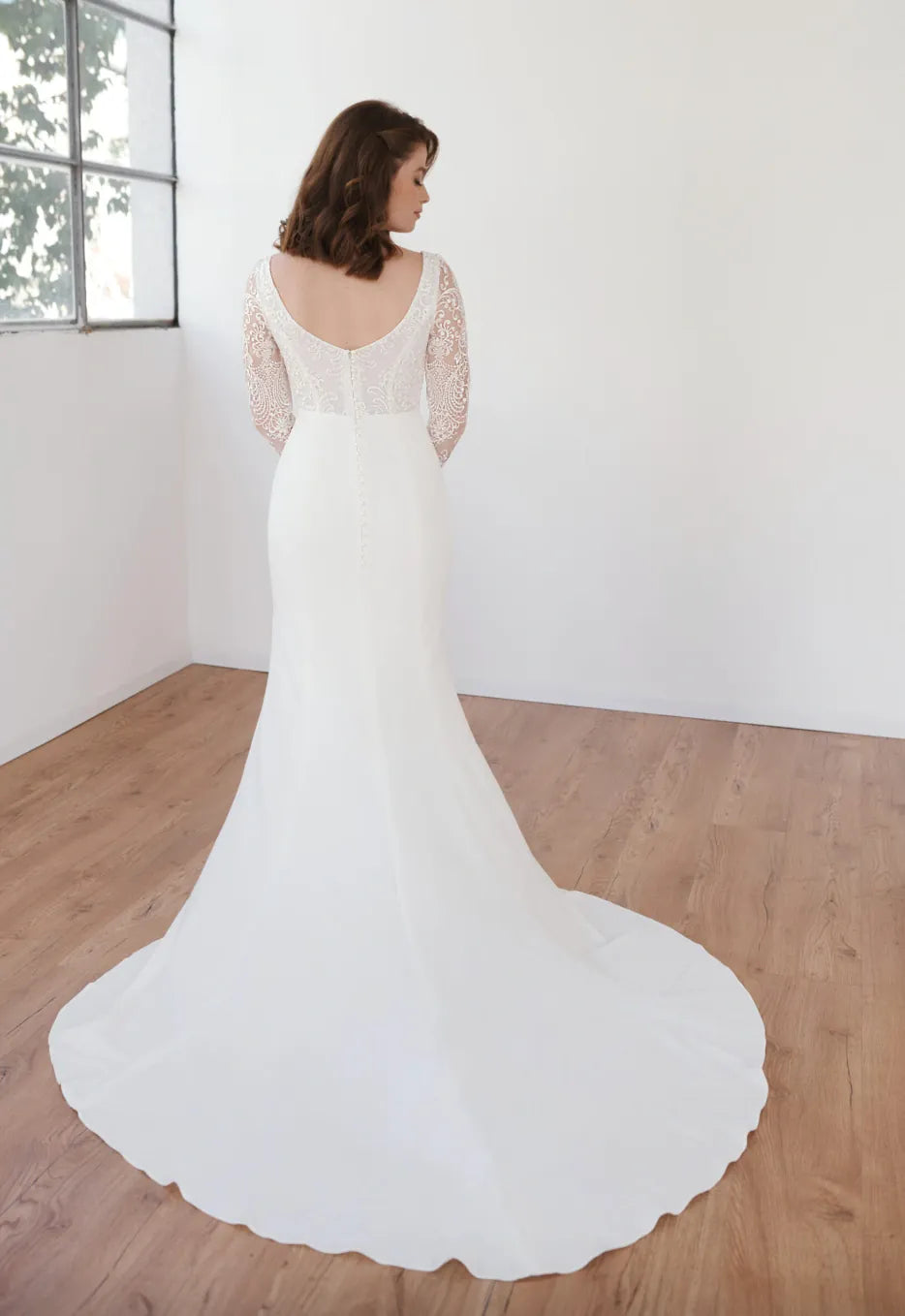 Woman wearing a white wedding dress with a long train in a minimalistic room.