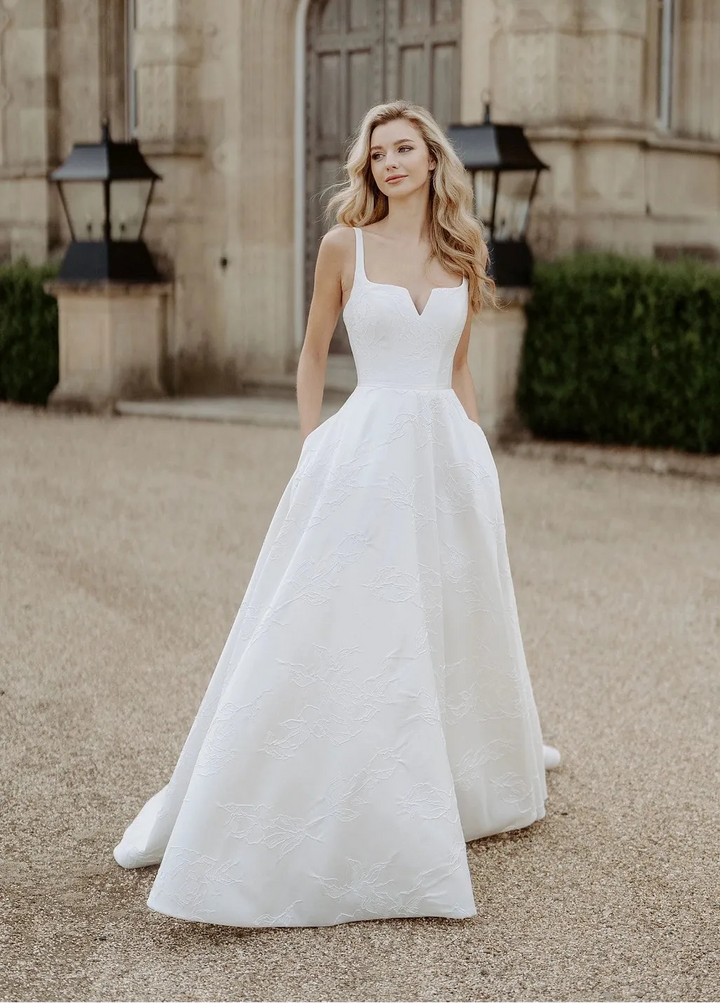 full front of suzanne neville bloomsbury ivory cloque a-line wedding dress with notched square neckline and skirt with pockets