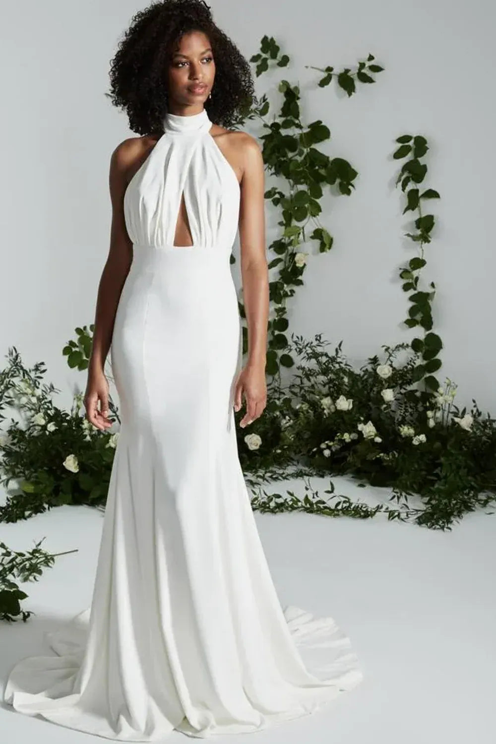 Woman in a white halter neck gown standing against a floral backdrop
