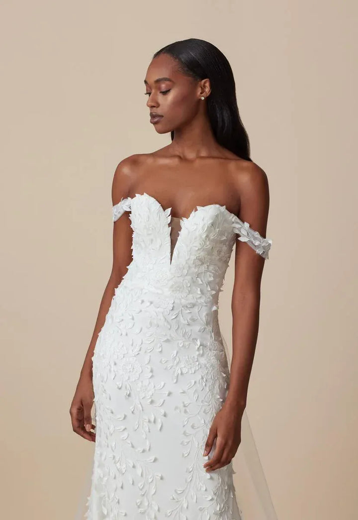 close up of ti adora maya ivory crepe fitted wedding dress with floral lace embellishments and an off the shoulder neckline