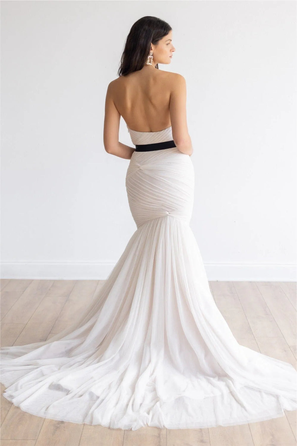 Woman wearing a white gown with a black belt on a plain background