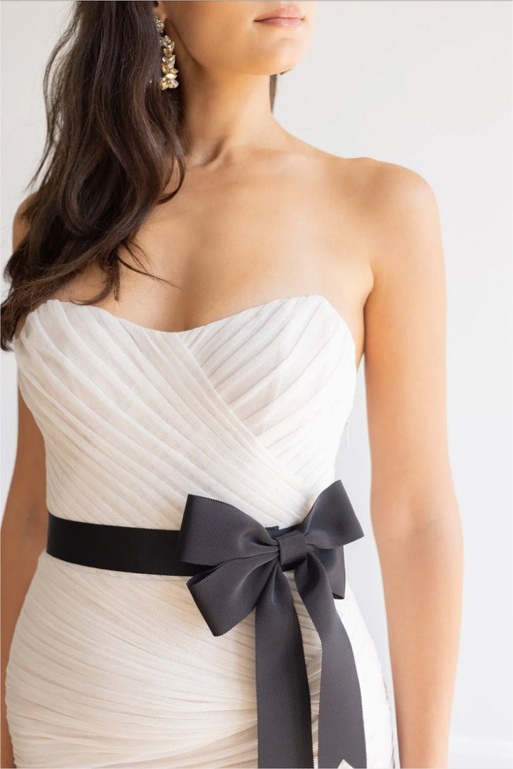 White strapless dress with a black ribbon bow on a plain background