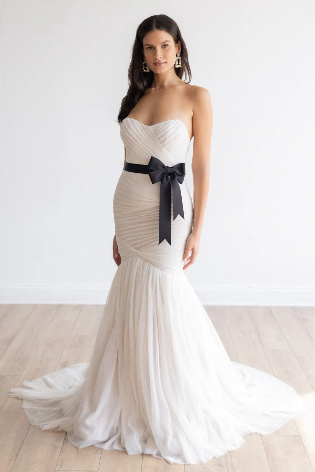 Woman wearing a white strapless gown with a black bow on a light wooden floor.