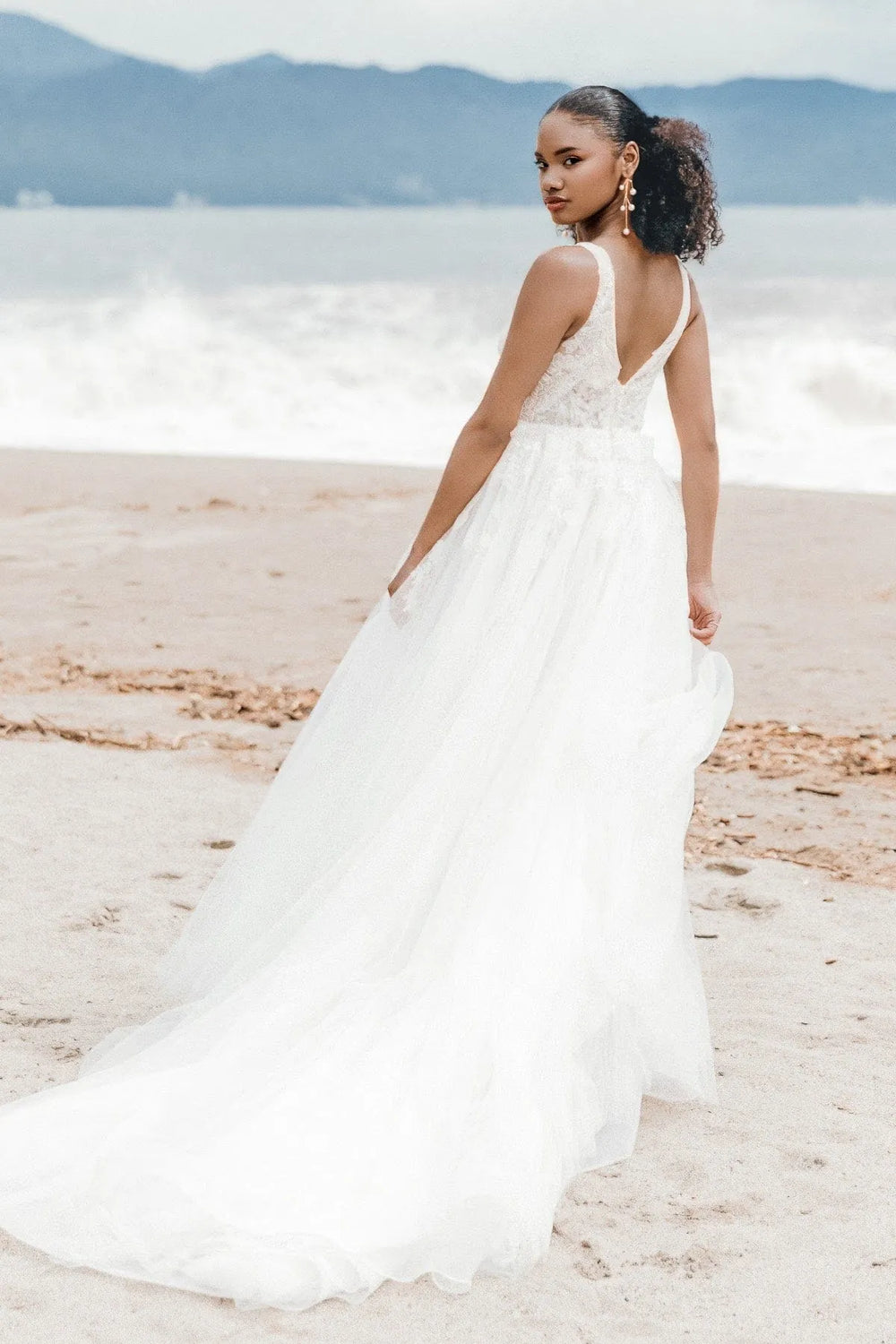 Woman in a white wedding dress standing on a beach with mountains in the background