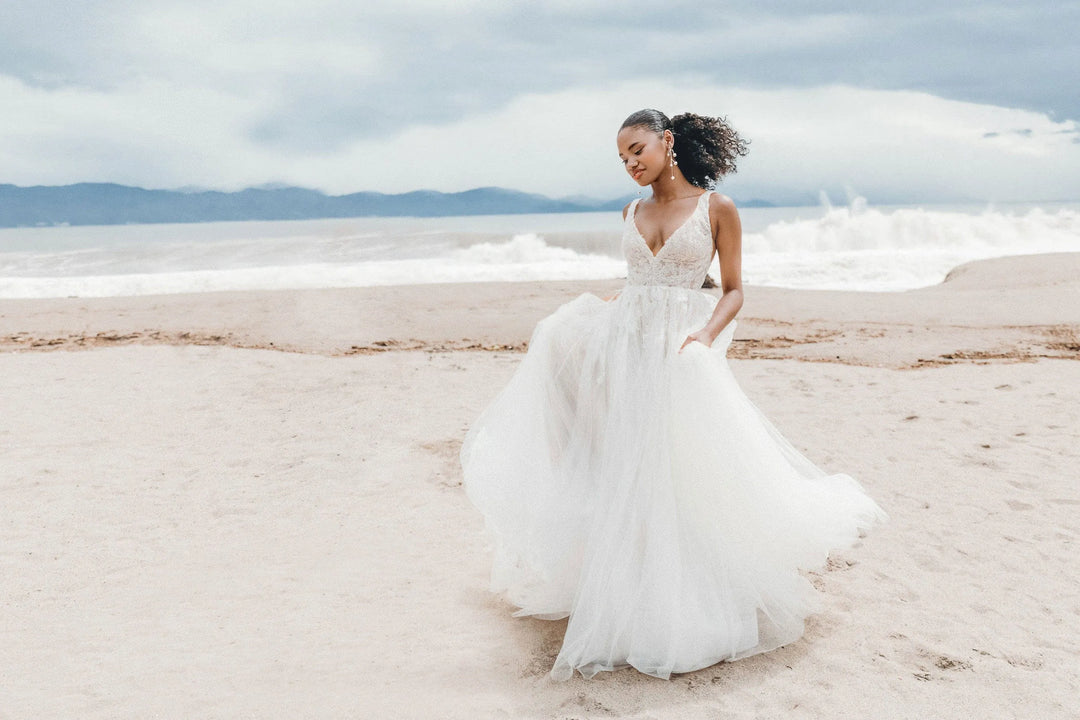Woman in a white wedding dress standing on a beach with ocean and sky in the background