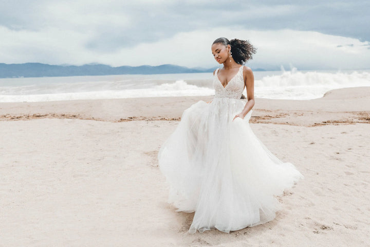 Woman in a white wedding dress standing on a beach with ocean and sky in the background