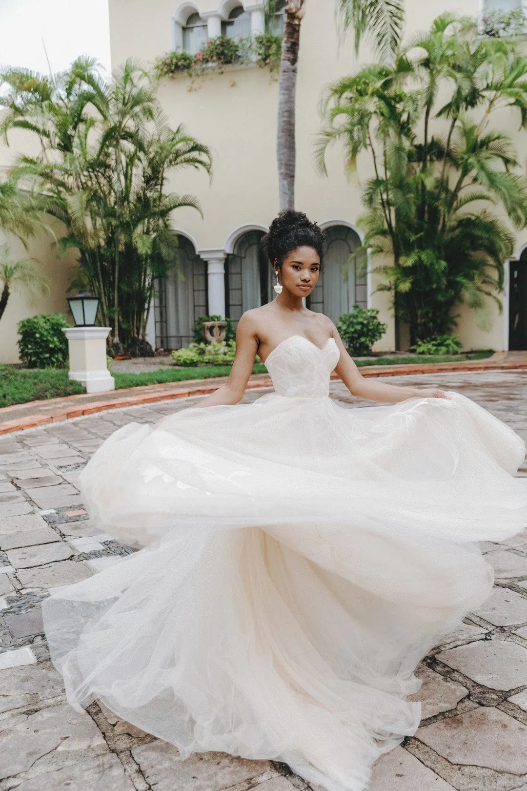 Woman in a white wedding dress standing in front of a building with palm trees.