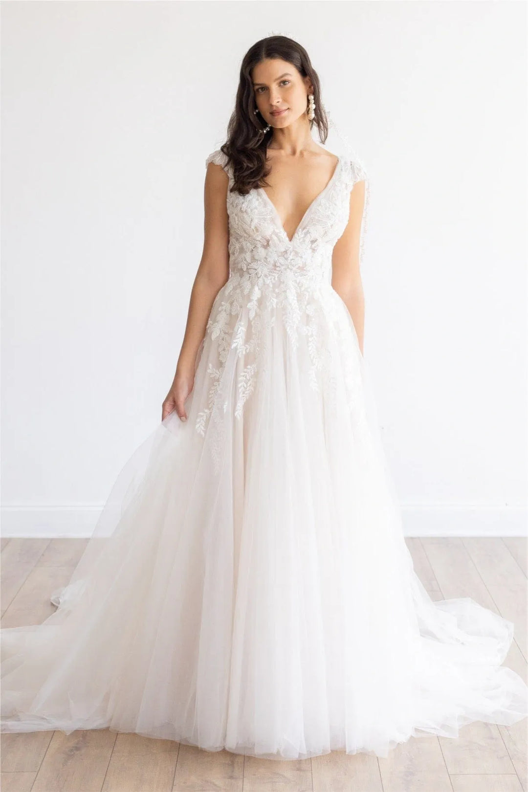 Woman wearing a white wedding dress with floral details against a plain background