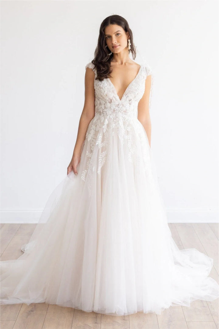 Woman wearing a white wedding dress with floral details against a plain background