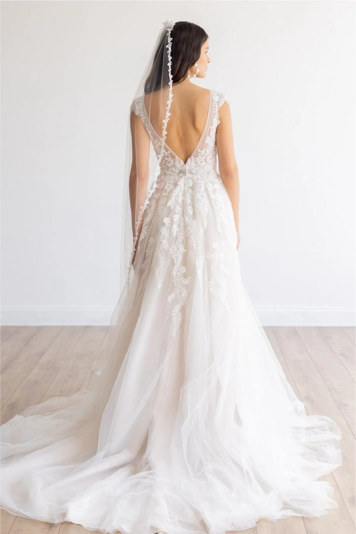 White wedding dress with a long train and lace detailing on a plain background