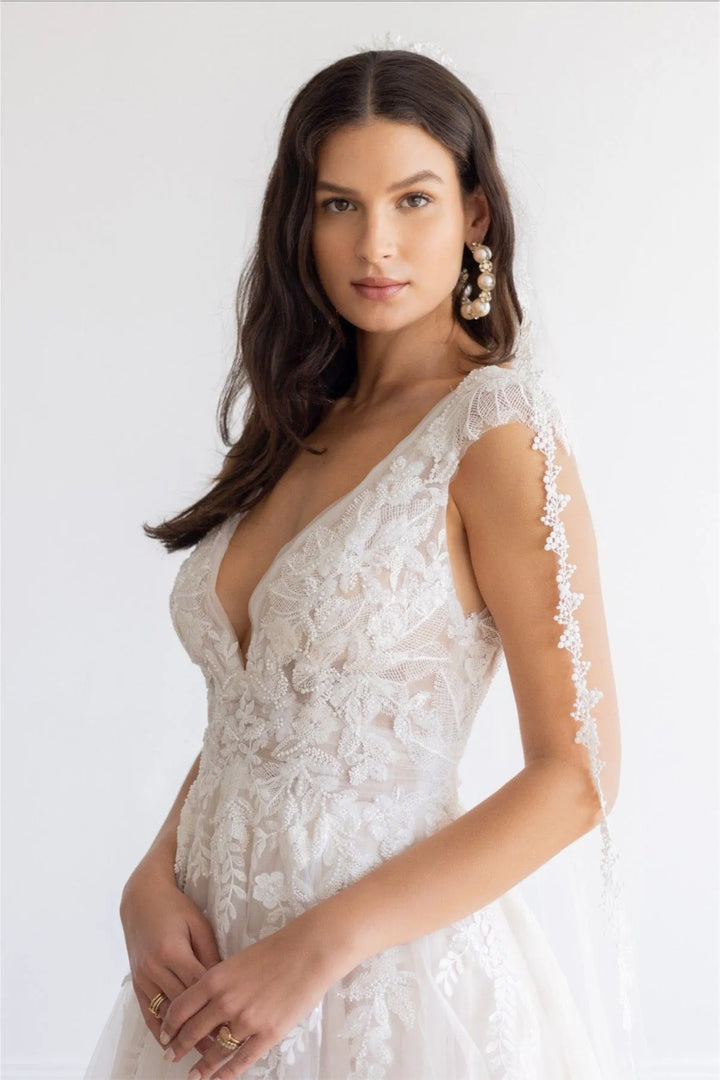 Woman wearing a white lace wedding dress against a plain background
