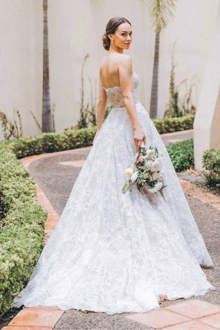 Woman in a white wedding dress holding flowers outdoors.