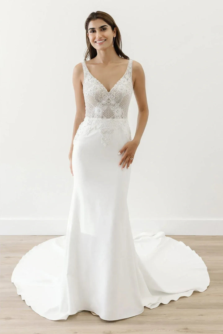 Woman wearing a white wedding dress with lace detailing on a light wooden floor.