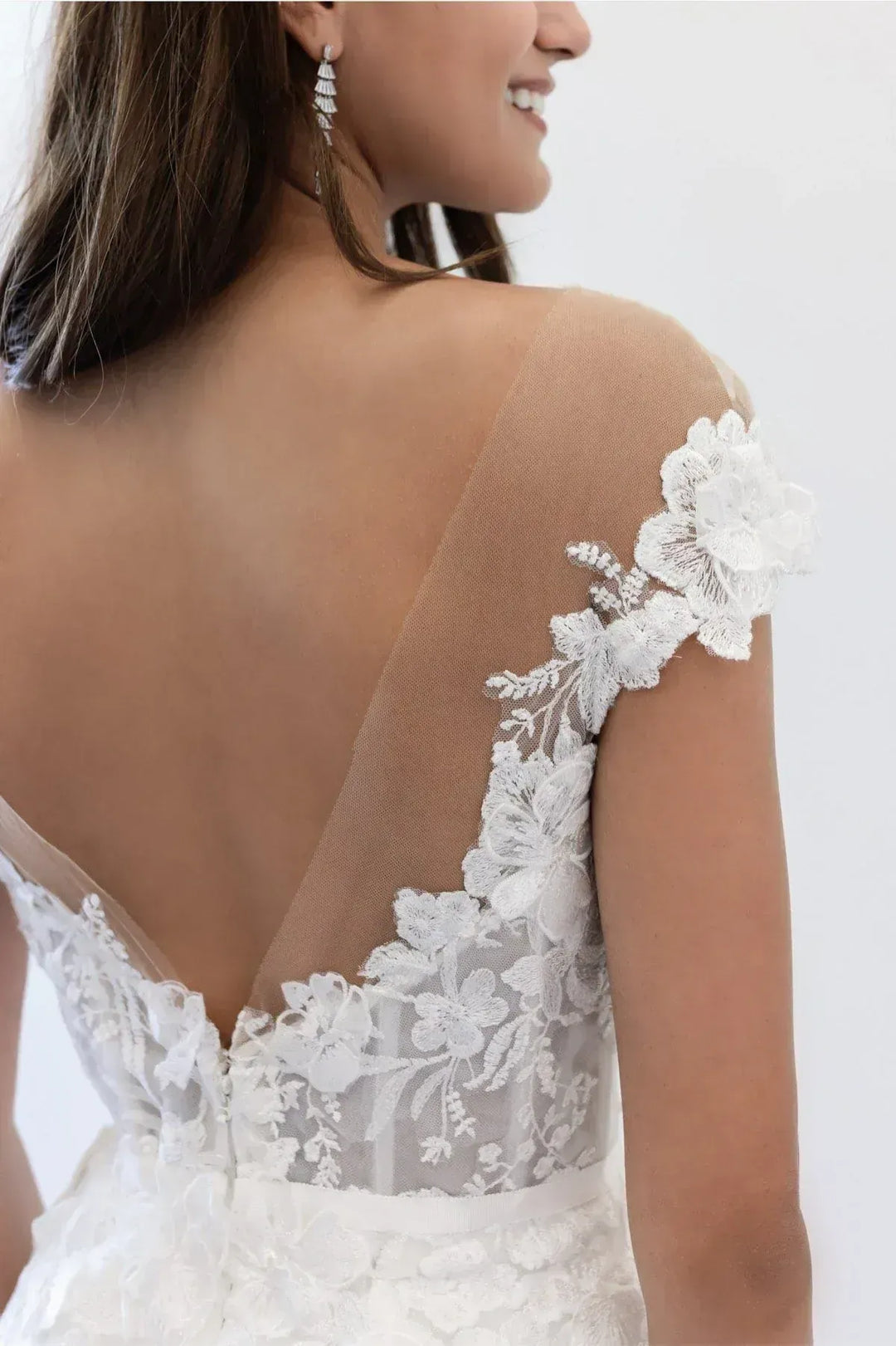 Close-up of a woman wearing a white lace wedding dress with floral details on a plain background