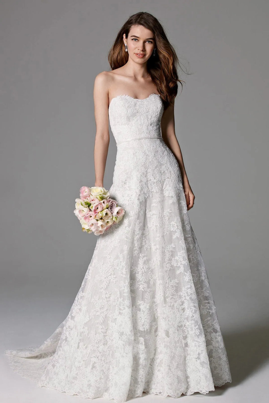 Woman wearing a strapless lace wedding dress holding flowers against a gray background