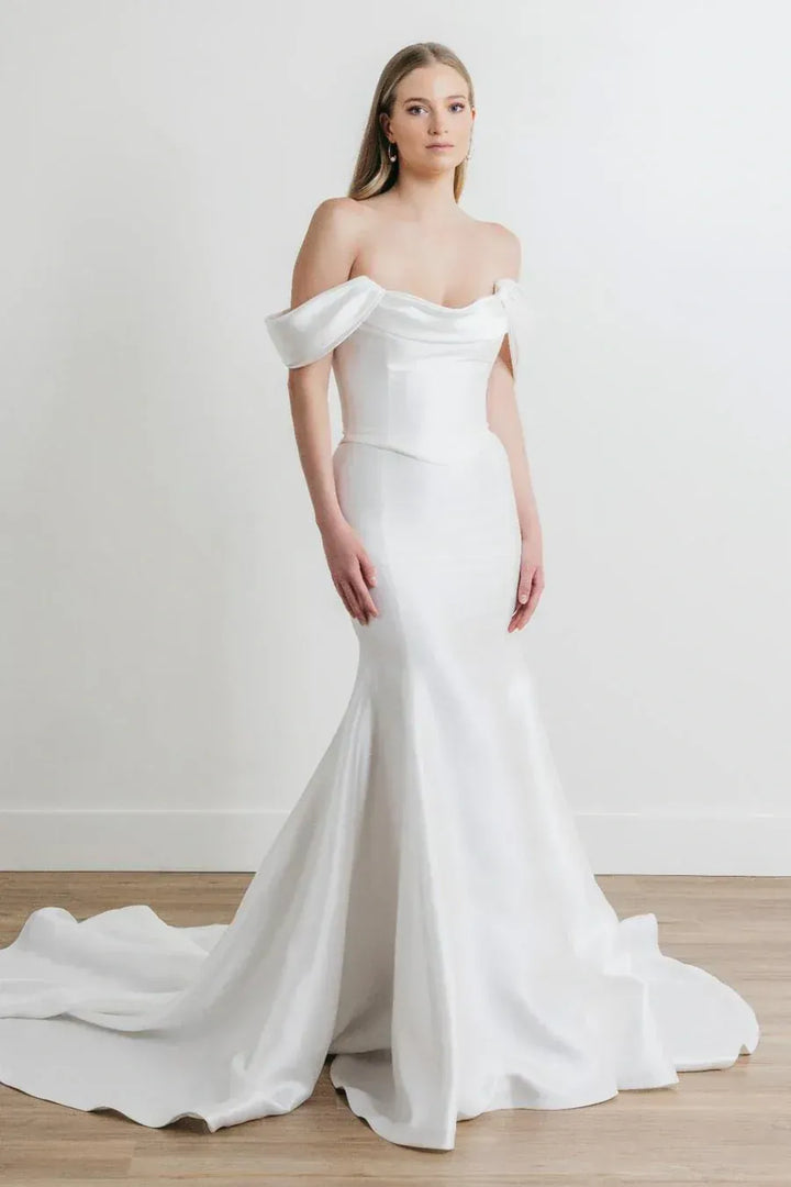 Woman wearing a white off-shoulder wedding dress on a plain background