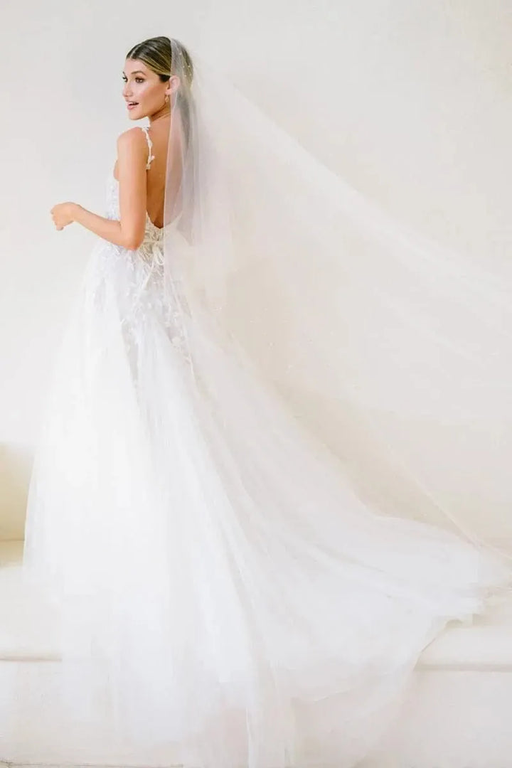 Woman in a white wedding dress with a long train against a plain background