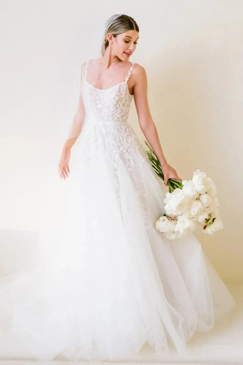 Bride in a white wedding dress holding a bouquet against a plain background