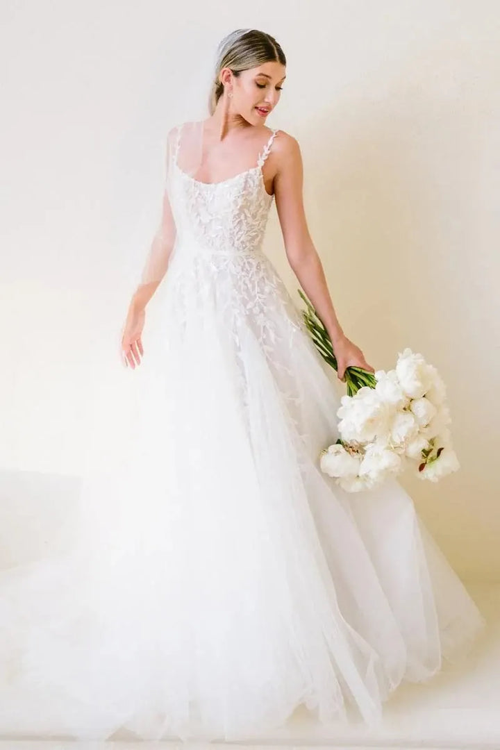 Bride in a white wedding dress holding a bouquet against a plain background