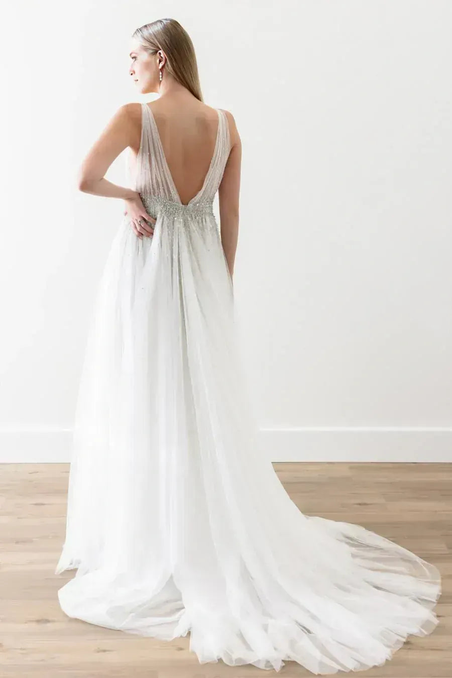 Woman wearing a white wedding dress with a long train on a wooden floor.