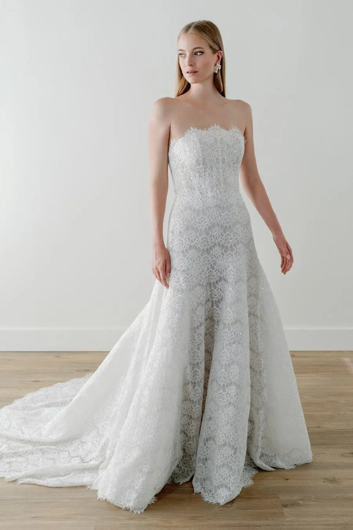 Woman wearing a strapless lace wedding dress with a slit on a wooden floor.