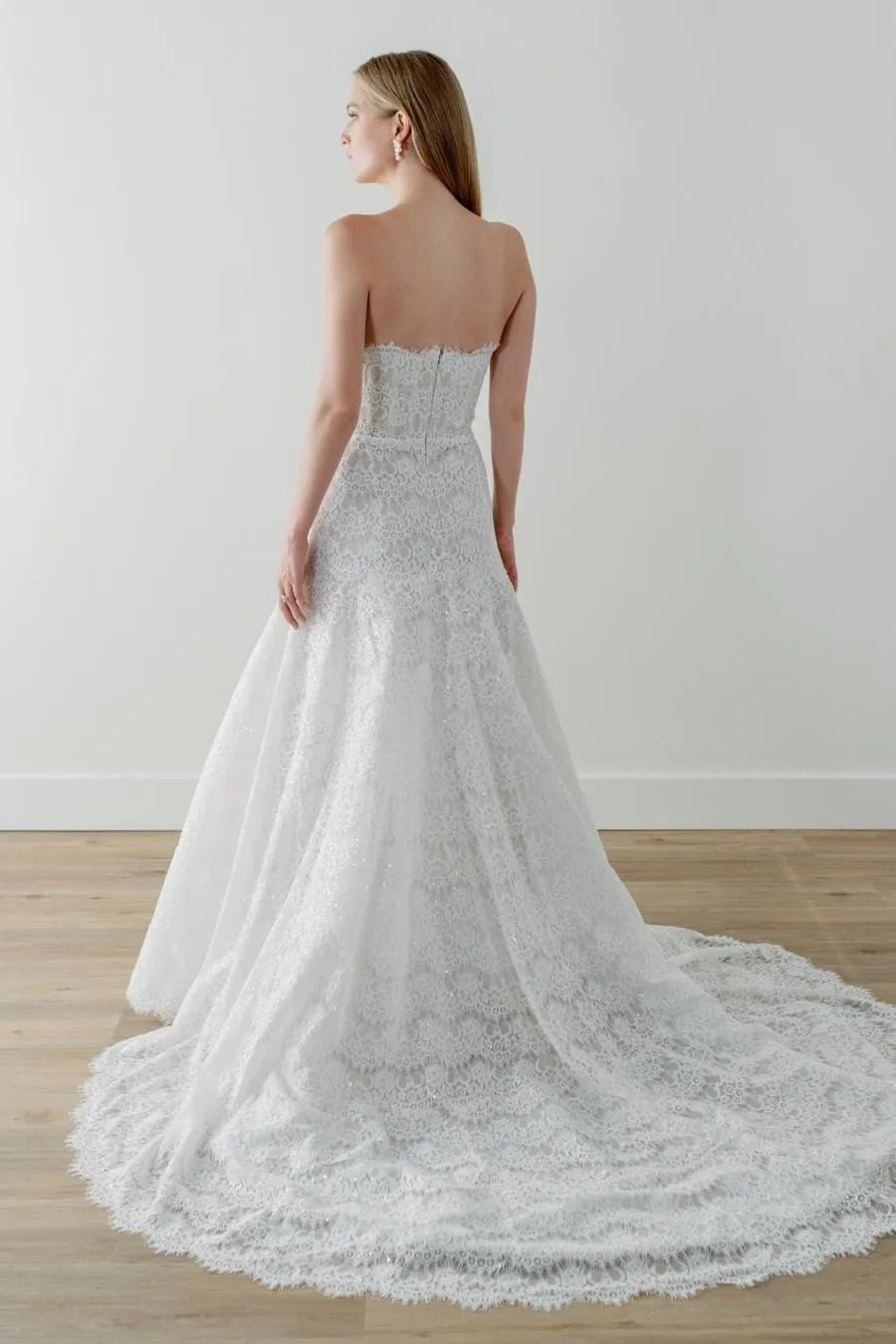 Woman wearing a strapless lace wedding dress on a plain background