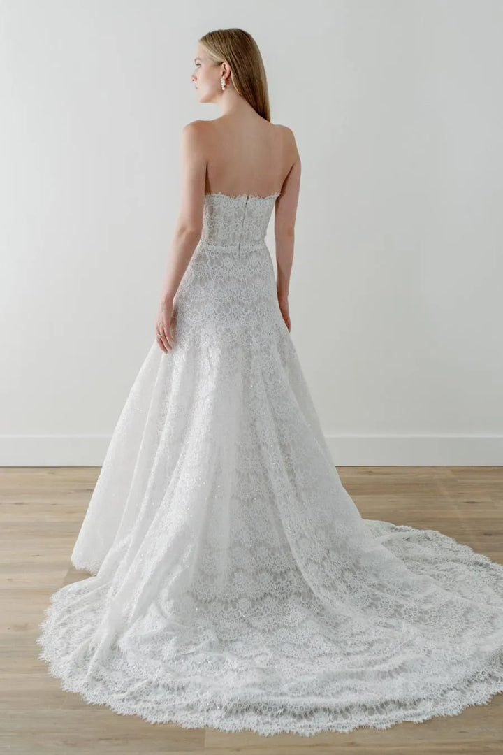 Woman wearing a strapless lace wedding dress on a plain background