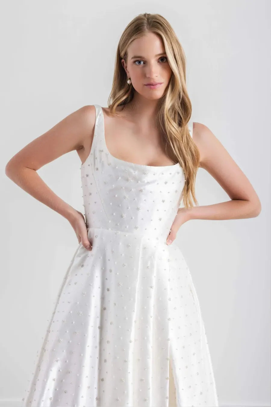 A blonde woman modeling a white sleeveless A-line dress with a dotted texture, standing against a light gray studio background.