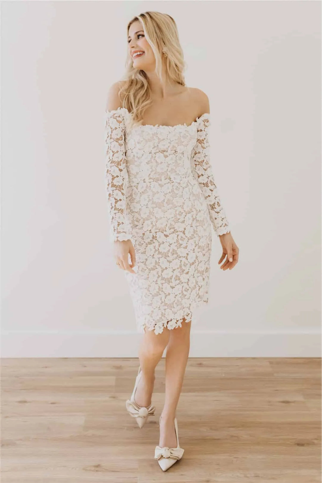 Woman wearing a white lace dress with long sleeves on a wooden floor.