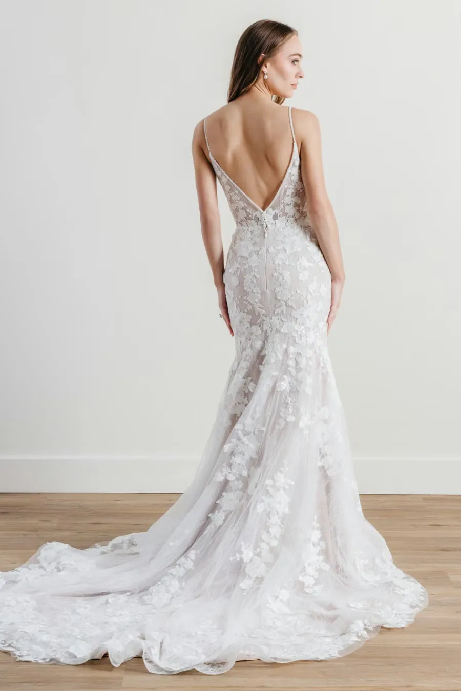 Woman wearing a white lace wedding dress with a low back on a plain background