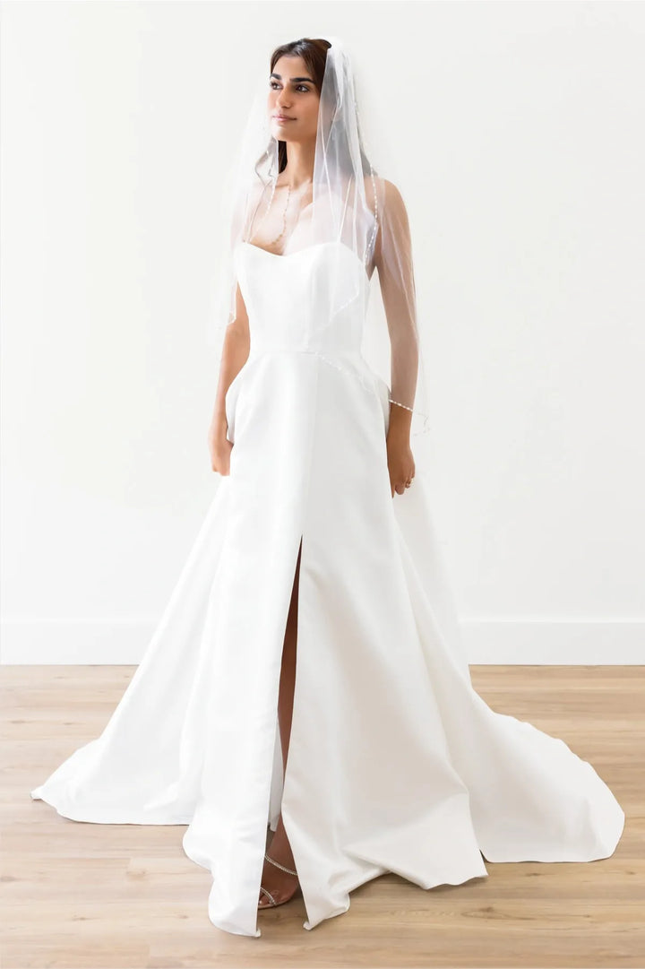 Woman wearing a white wedding dress with a long train on a wooden floor.