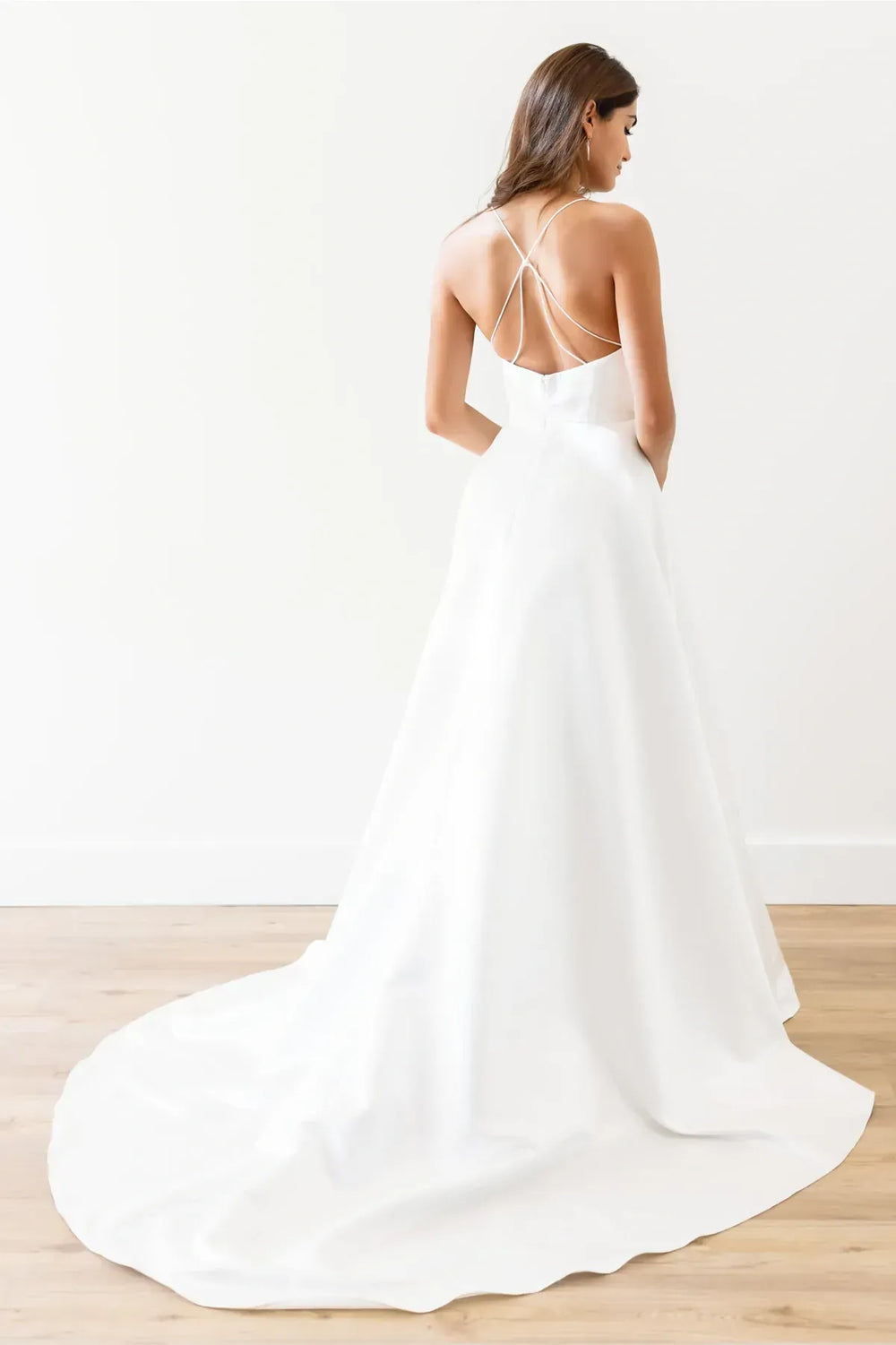 Woman wearing a white wedding dress with thin straps on a wooden floor.