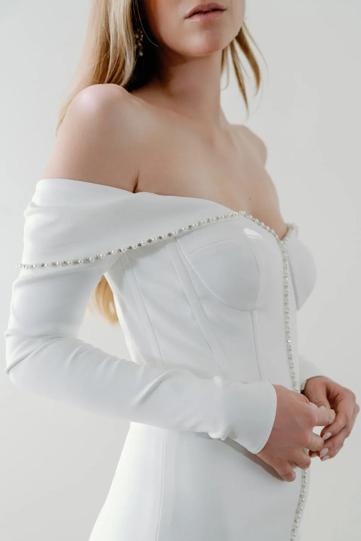 close up of watters everette ivory crepe fitted wedding dress with an off the shoulder long sleeve neckline trimmed with pearls
